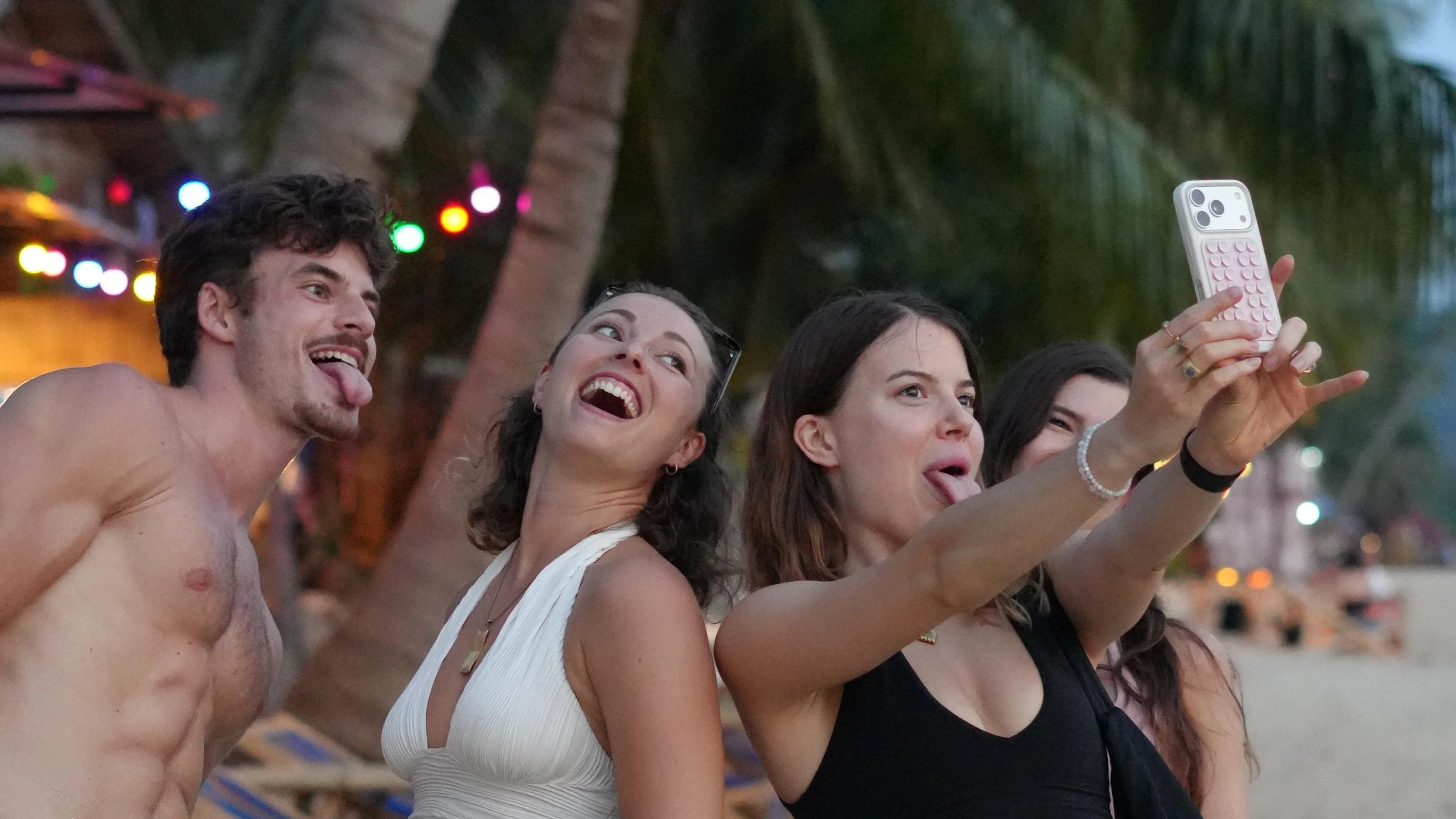 Gruppe macht abends am Strand unter Palmen ein Selfie