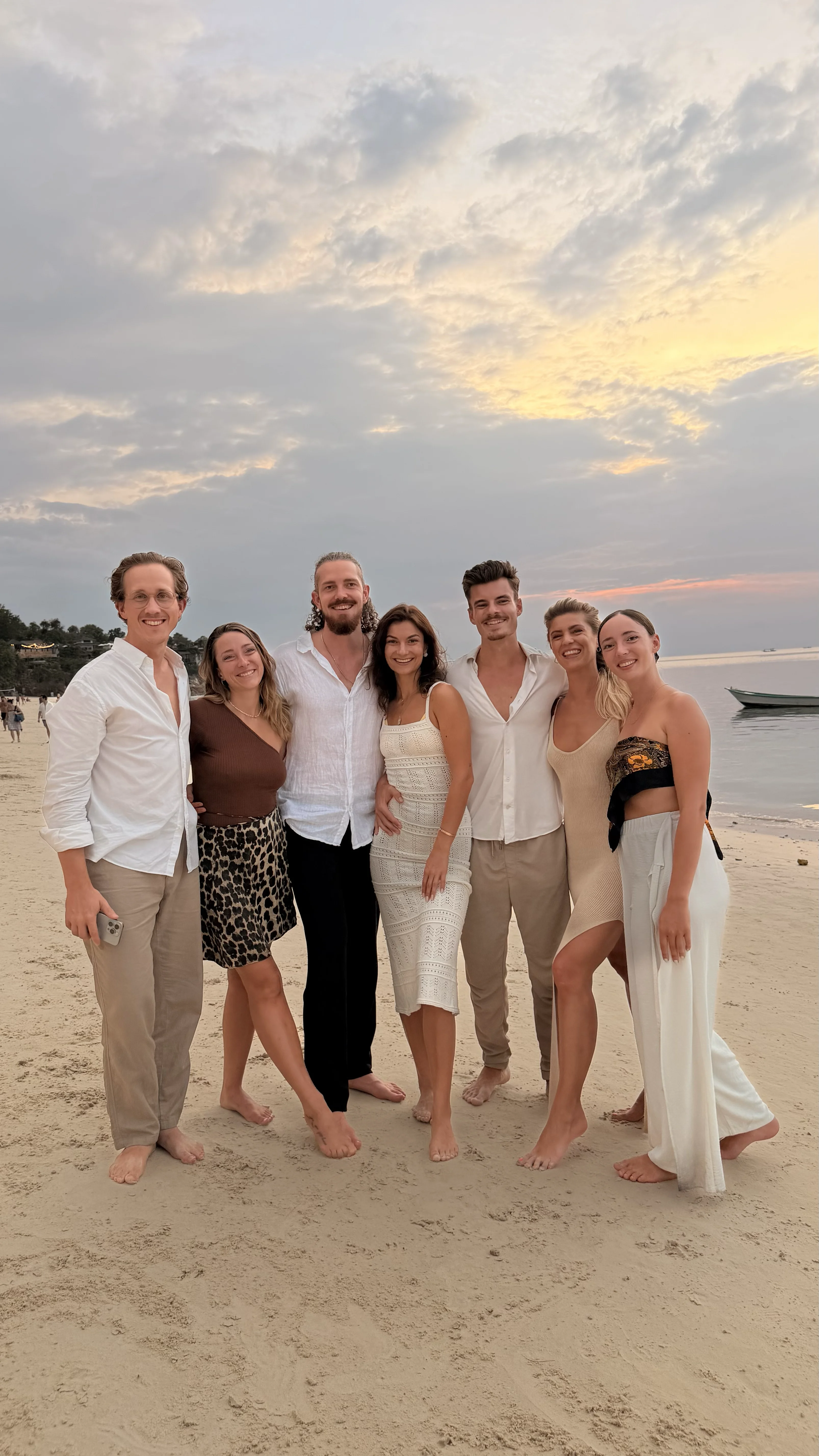Sieben Freunde stehen lächelnd am Strand von Koh Phangan bei Sonnenuntergang