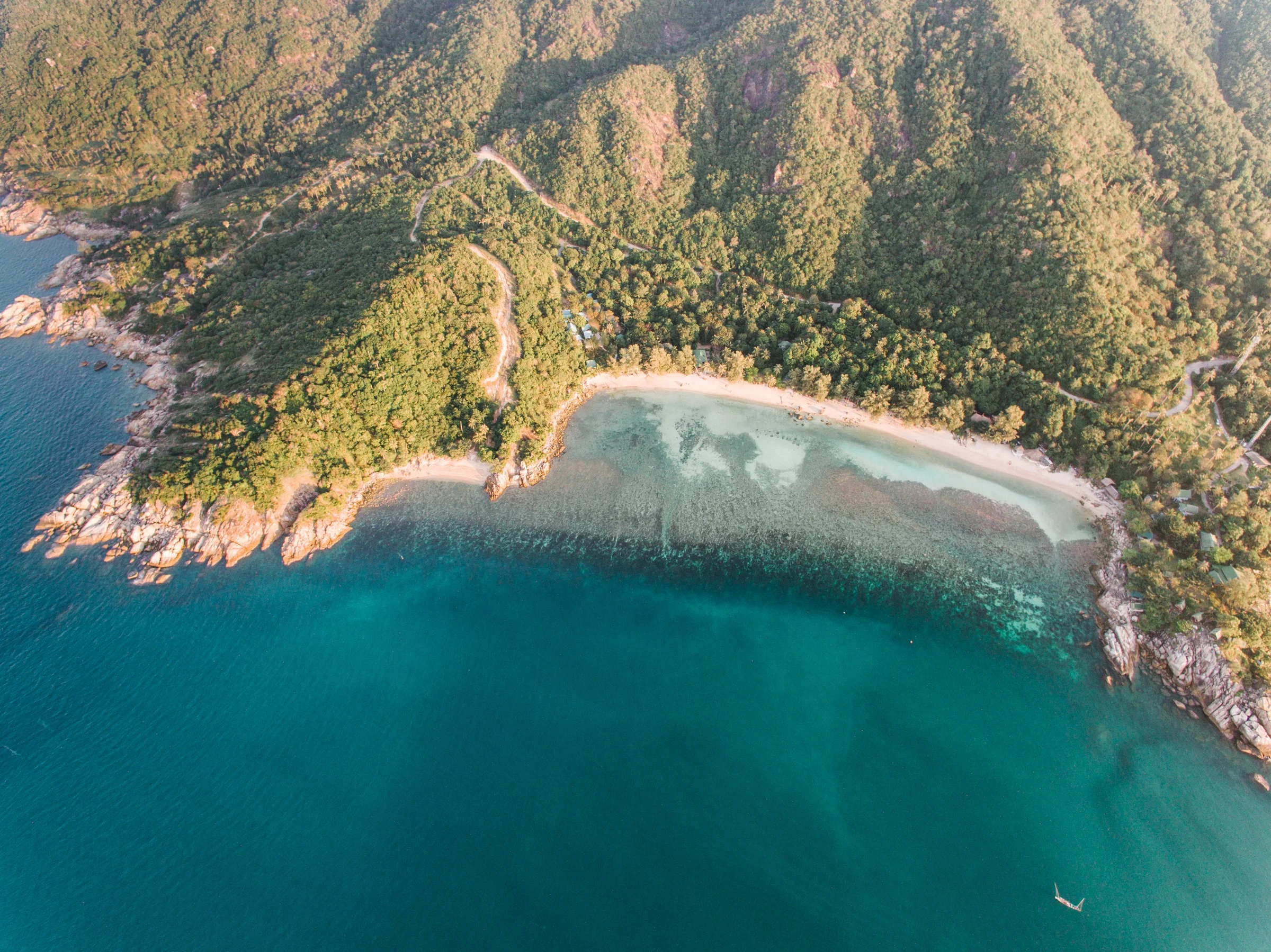 Luftaufnahme einer Bucht auf Koh Phangan mit Korallenriff, türkisem Wasser und Dschungel